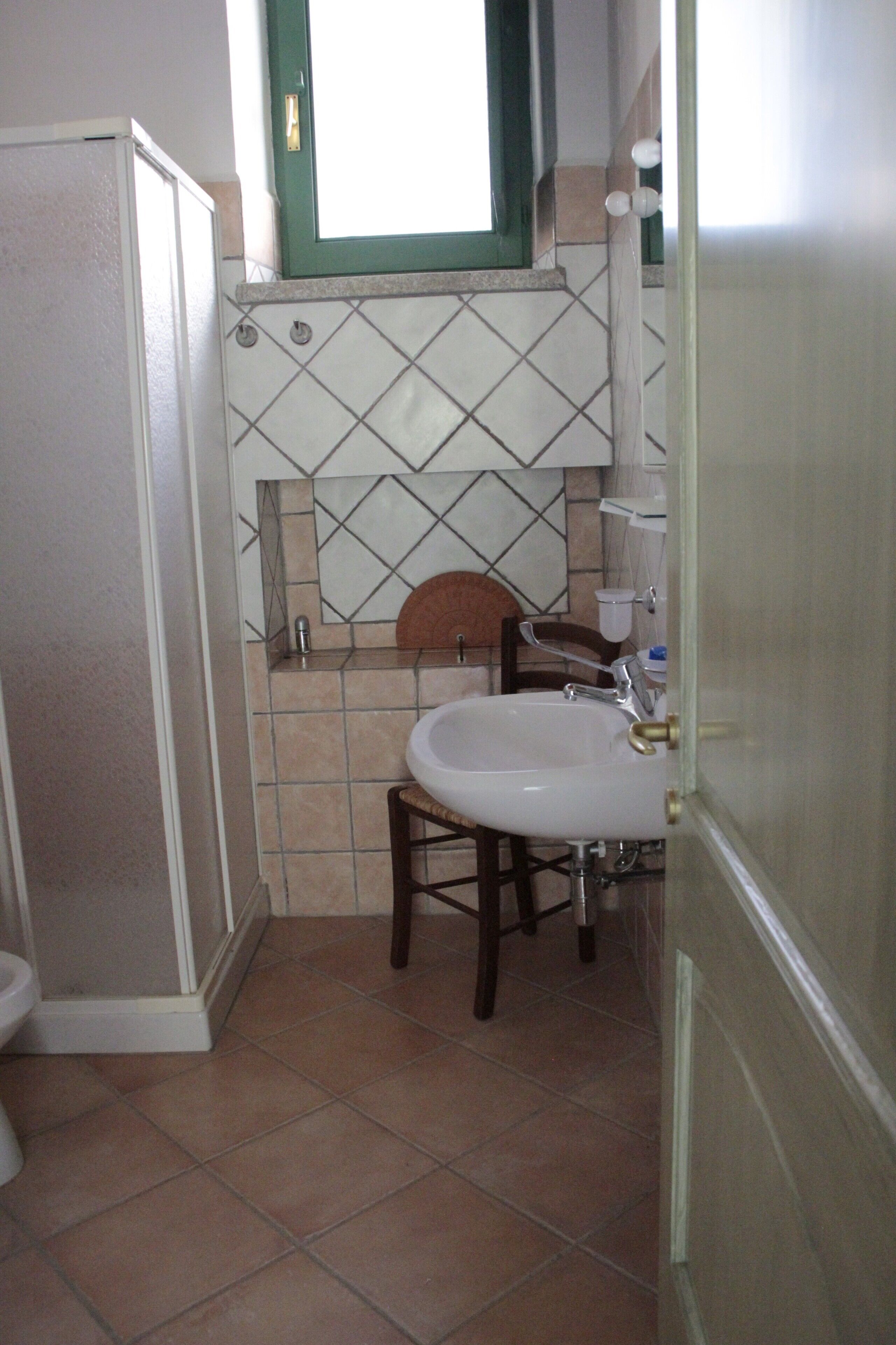 A bathroom with a sink, chair, and a window above the mirror.