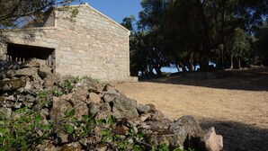 A stone building with a small entrance, surrounded by a stone wall and vegetation. - Cottage 'Stazzu Spadulagliu near Olbia' with Mountain View, Wi-Fi and Air Conditioning (Telti)