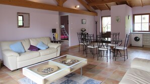 A spacious living area with a high ceiling, a sofa, a coffee table, a dining table with chairs, and a washing machine. - Lavender Cottage, Heated Pool, Between Countryside and Sea, Quiet Marais Poitevin Retreat (Nalliers)