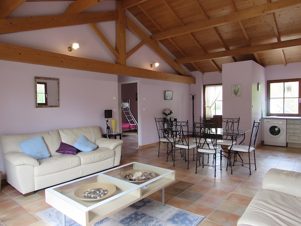 A spacious living area with a high ceiling, a sofa, a coffee table, a dining table with chairs, and a washing machine.
