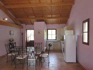 A kitchen with wooden beams, a dining table with chairs, a refrigerator, and a window with curtains.