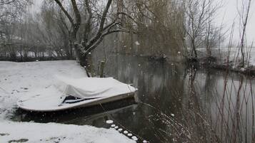 Un bateau recouvert d’une bâche blanche, amarré à un quai par une corde, avec de la neige au sol et des arbres en arrière-plan.