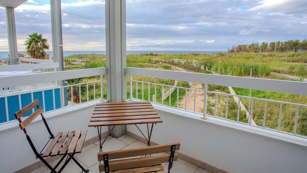 A balcony with a wooden table and chairs, overlooking a grassy landscape and the sea. - Sea Apartment (Nocera Terinese)