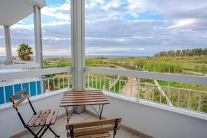 Un balcón con mesa y sillas de madera, con vistas a un paisaje cubierto de hierba y al mar.