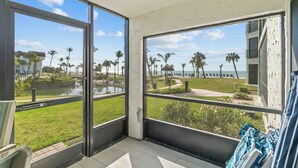 Un balcone con ampie finestre che si affaccia su una spiaggia con palme e un corpo d'acqua.