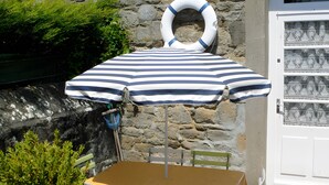 A table with a striped umbrella, a stone wall, and a door with patterned glass. - Holiday Home “Les Flots Bleus Cancale” with Private Terrace, Garden & Wi-Fi (Cancale)