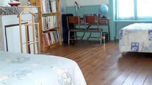 A room with a wooden bookshelf, a desk with a globe, two chairs, and a bed with floral bedding. - Holiday Home “Les Flots Bleus Cancale” with Private Terrace, Garden & Wi-Fi (Cancale)