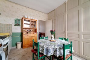 Uma sala de jantar com mesa redonda, cadeiras, um aparador com portas de vidro e um vaso com flores.