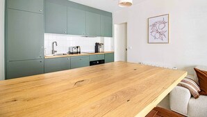 A modern kitchen with teal cabinets, a wooden countertop, and a white backsplash. - Sevres - Bright 2-bedroom near Bon Marché (Paris)