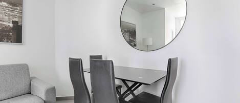 A modern room with a gray sofa, a dining table with four chairs, and a large round mirror on the wall.