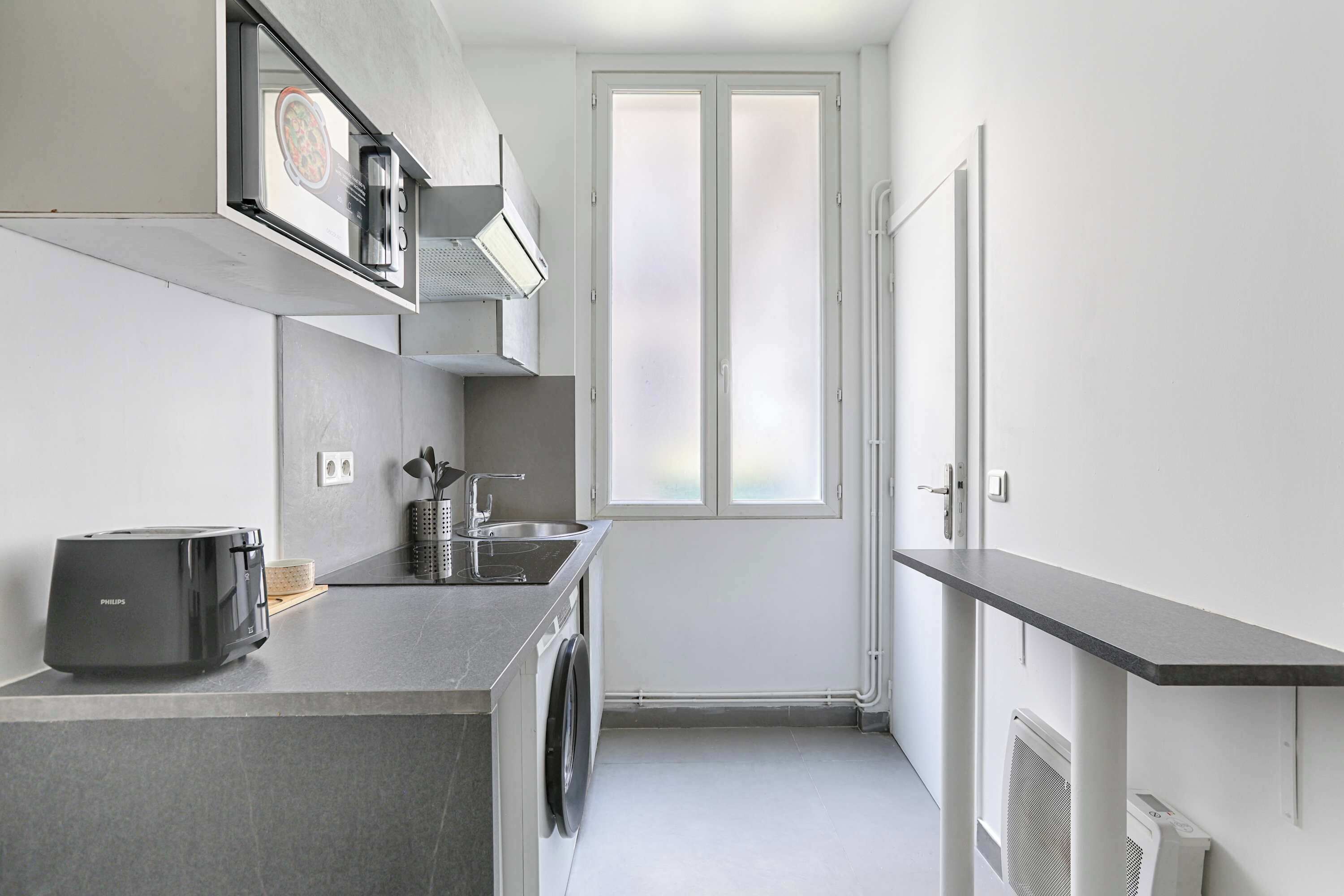 A compact kitchen with a washing machine, a toaster, and a small sink.