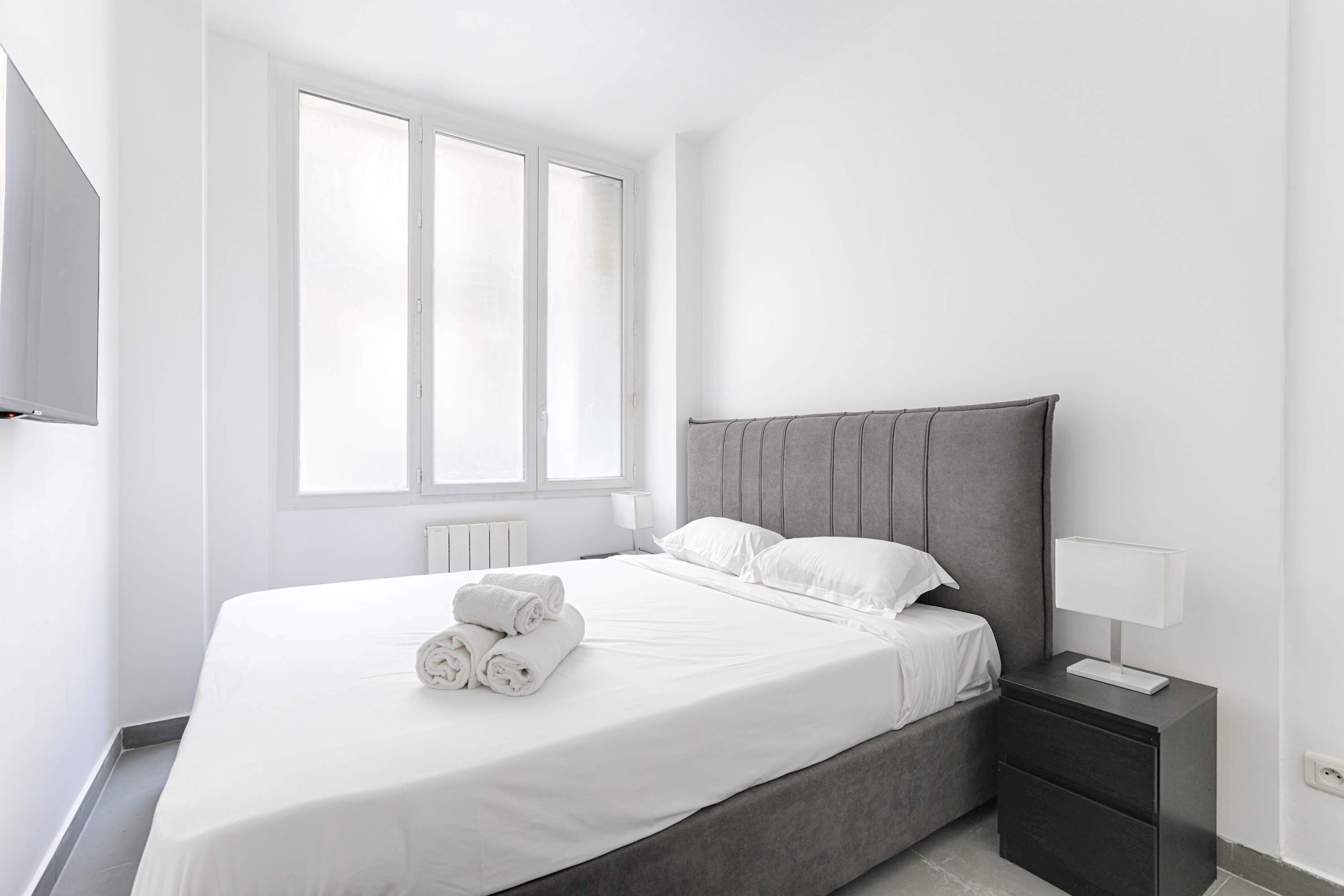 A modern bedroom with a large bed, a bedside table, and a window.
