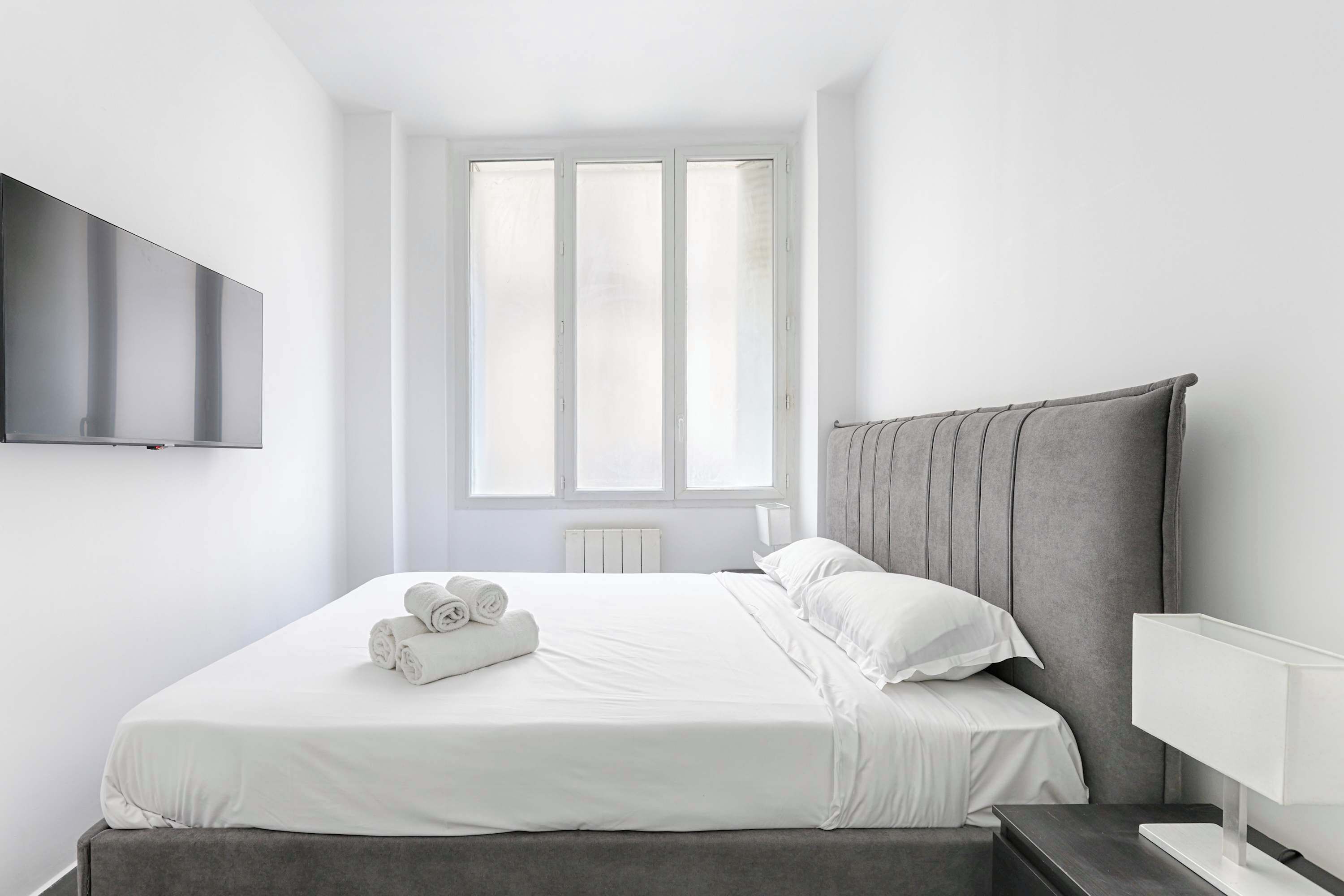 Ein modernes Hotelzimmer mit einem großen Bett, einem an der Wand befestigten Flachbildfernseher und einem Fenster mit vertikalen Jalousien.