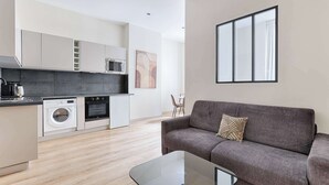 Un apartamento moderno con cocina, un sofá gris y un ventanal grande.