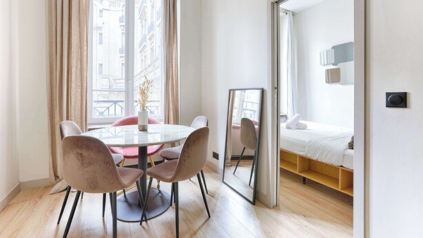 Una habitación moderna con una mesa redonda de comedor, cuatro sillas, una cama con cabecero de madera y un espejo grande.