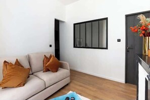En moderne stue med en beige sofa, en blå måtte og et spejl med sort ramme på væggen.