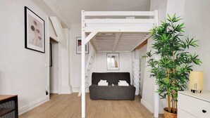 A room with a bunk bed, a grey sofa, a potted plant, and a white dresser. - Appartement cosy avec jardin proche de République (Paris)