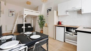 A compact kitchen with white cabinets, a built-in oven, and a small refrigerator. - Appartement cosy avec jardin proche de République (Paris)