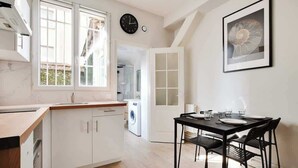 A modern kitchen with white cabinets, a wooden countertop, and a dining area with a black table and chairs. - Appartement cosy avec jardin proche de République (Paris)