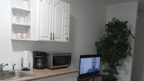 Una cocina con armarios blancos, microondas, cafetera y televisor sobre un soporte.