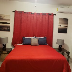Ein Schlafzimmer mit rotem Überwurf, zwei Kissen, einem roten Vorhang und zwei Nachttischen mit Lampen.