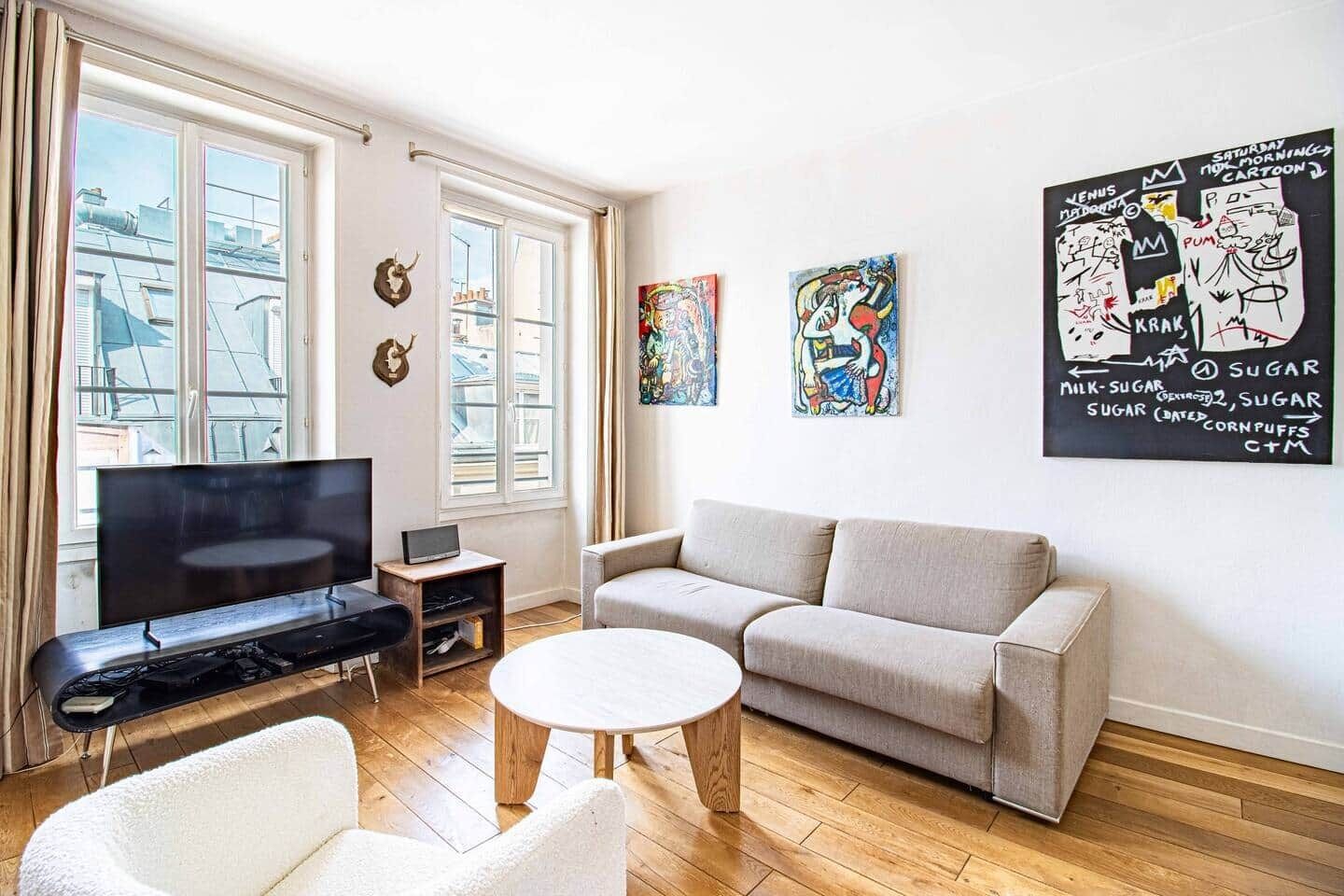Un salon avec un canapé, une table basse, un téléviseur et des œuvres d’art accrochées aux murs.
