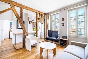 En moderne stue med træbjælke-konstruktion, et fjernsyn, en sofa og et spiseområde med bord og stole.