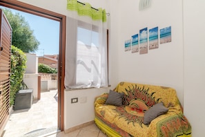 A room with a sofa, a window with a curtain, and a wall with framed pictures. - San Teodoro Monti 22 – 20 minutes’ walk to the beach, private terrace & air conditioning (San Teodoro)