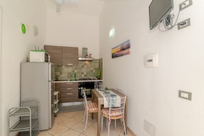 A compact kitchen with a dining table, chairs, a refrigerator, a stove, and a microwave. - San Teodoro Monti 22 – 20 minutes’ walk to the beach, private terrace & air conditioning (San Teodoro)