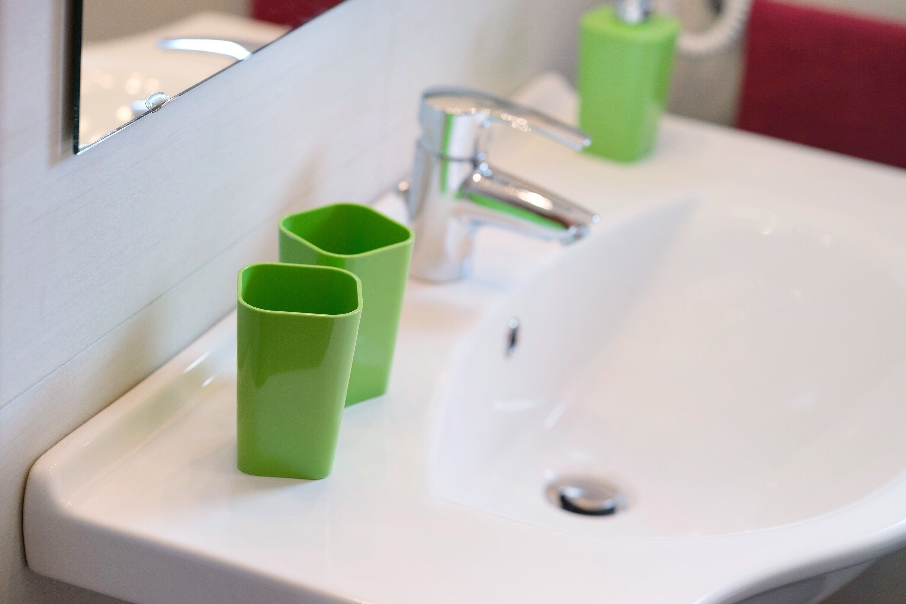 Un lavamanos blanco con grifo cromado, dos dispensadores de jabón verde y un espejo que refleja parte del baño.