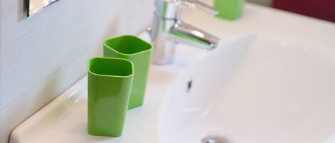 Un lavamanos blanco con grifo cromado, dos dispensadores de jabón verde y un espejo que refleja parte del baño.