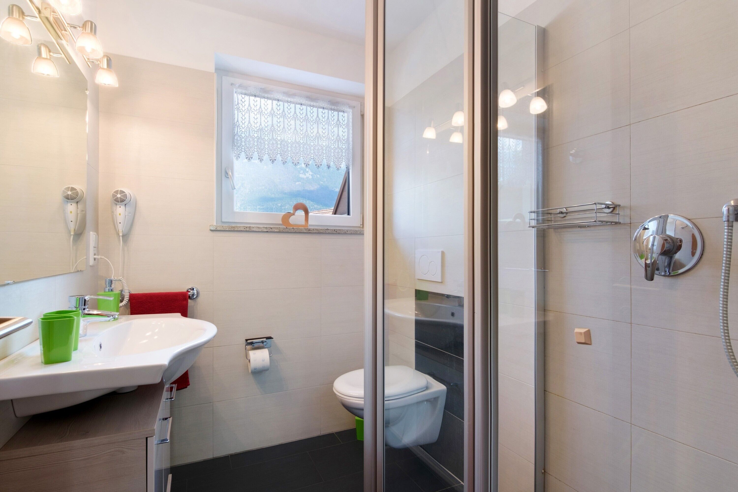 A modern bathroom with a glass shower enclosure, a white sink with green cups, and a toilet.