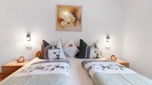 Una cama doble con ropa de cama floral, dos mesitas de noche, una lámpara de pared y una obra de arte floral enmarcadas.