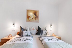 Ein Doppelbett mit floraler Bettwäsche, zwei Nachttische, eine an der Wand befestigte Lampe und ein gerahmtes Blumenbild.