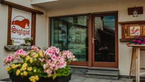 Une entrée d’immeuble avec une enseigne indiquant « Siglgut », un banc en bois et un pot de fleurs.