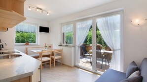 Une cuisine moderne dotée d’un four encastré, un coin repas avec une table et des chaises, et une porte-fenêtre coulissante donnant sur une terrasse extérieure.