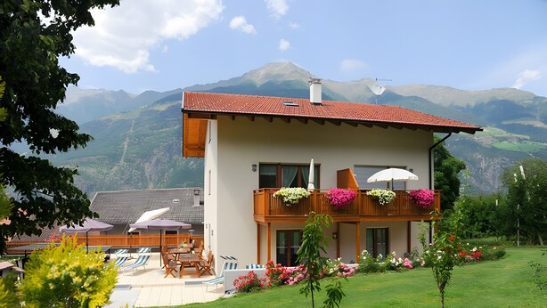 Une maison à deux étages dotée d’un balcon, d’un patio aménagé avec du mobilier d’extérieur et surplombant un paysage montagneux.