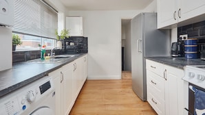 A modern kitchen with white cabinets, a stainless steel refrigerator, a dishwasher, and a coffee maker. - Ladykirk Road (Newcastle-upon-Tyne)