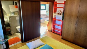 A bedroom with a bed, pillows, a wardrobe, a bathroom with a sink and mirror, and a small seating area with a chair and table. - Apartment Anglet Chiberta, beaches, surf, golf, parking, air conditioning (Anglet)