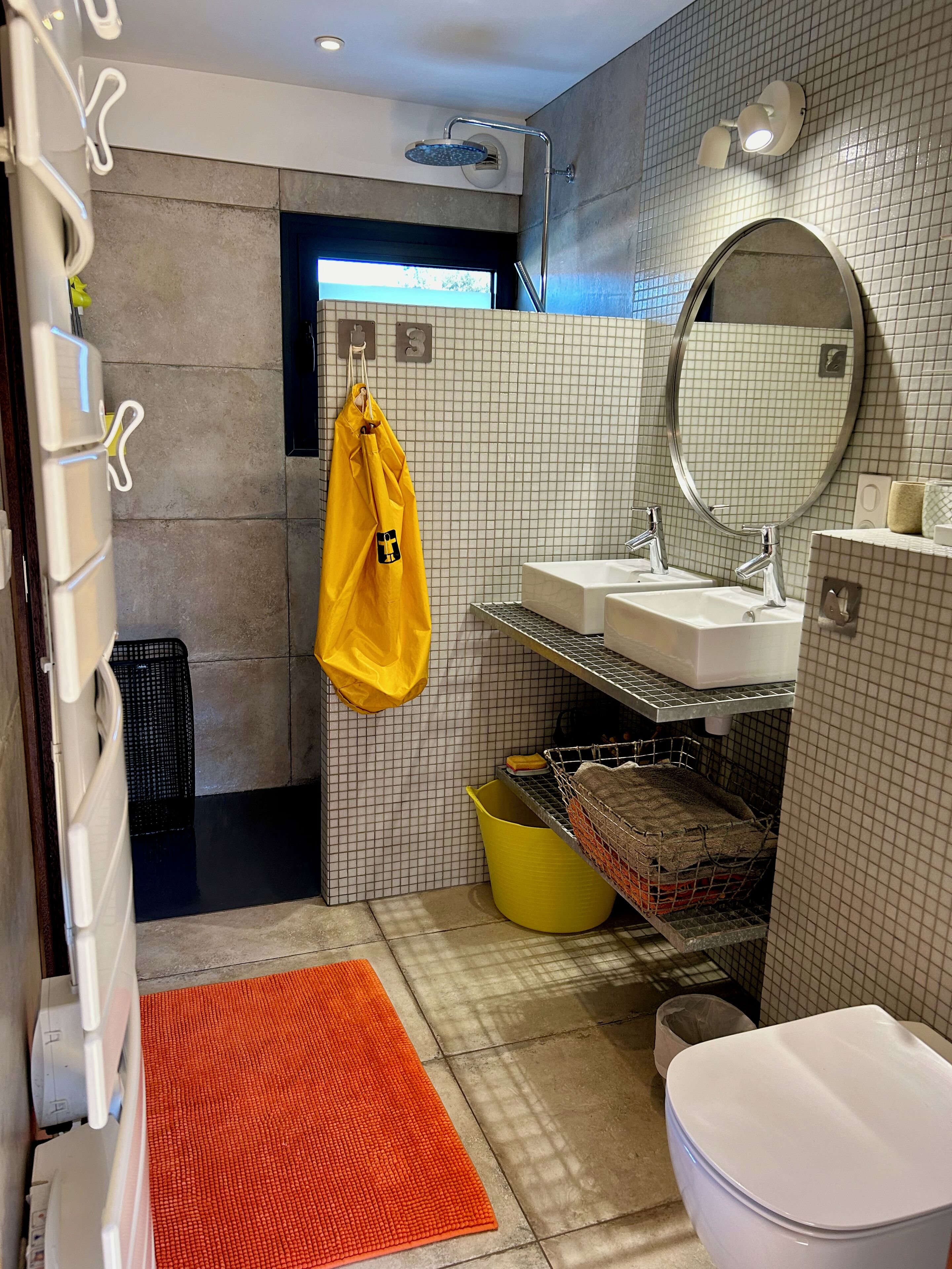 A modern bathroom with a shower, two sinks, a mirror, and a yellow towel hanging on a rack.