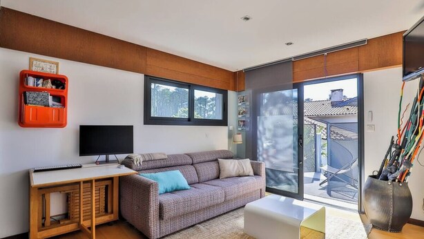 A modern living room with a sofa, a desk, a TV, and a sliding glass door leading to an outdoor area. - Apartment Anglet Chiberta, beaches, surf, golf, parking, air conditioning (Anglet)