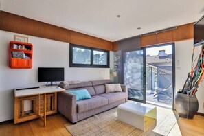Un salon moderne comprenant un canapé, un bureau, un téléviseur et une porte-fenêtre coulissante donnant sur un espace extérieur.