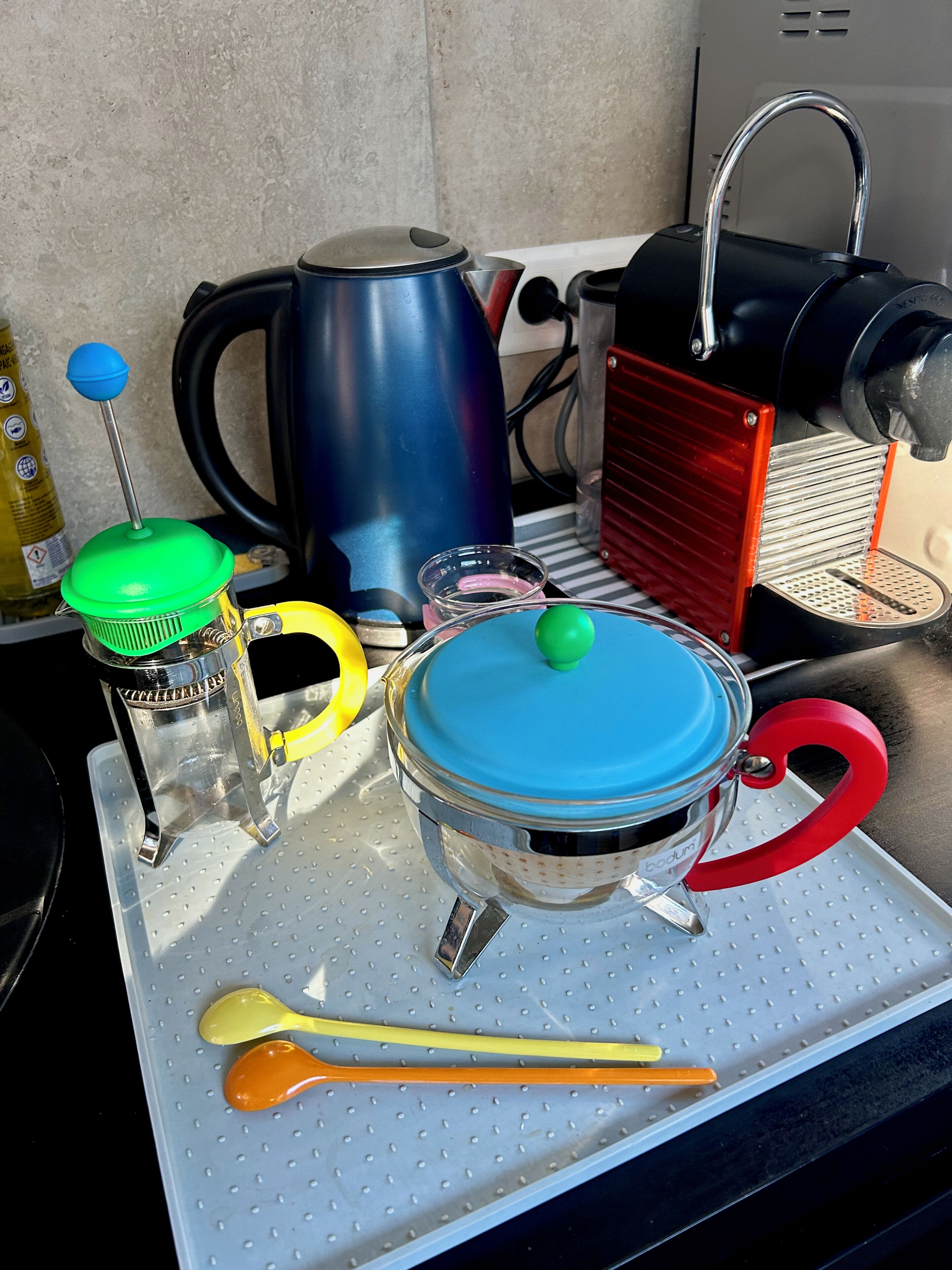 Uma bancada de cozinha com diversos eletrodomésticos, incluindo uma cafeteira, uma chaleira e um espremedor de frutas.