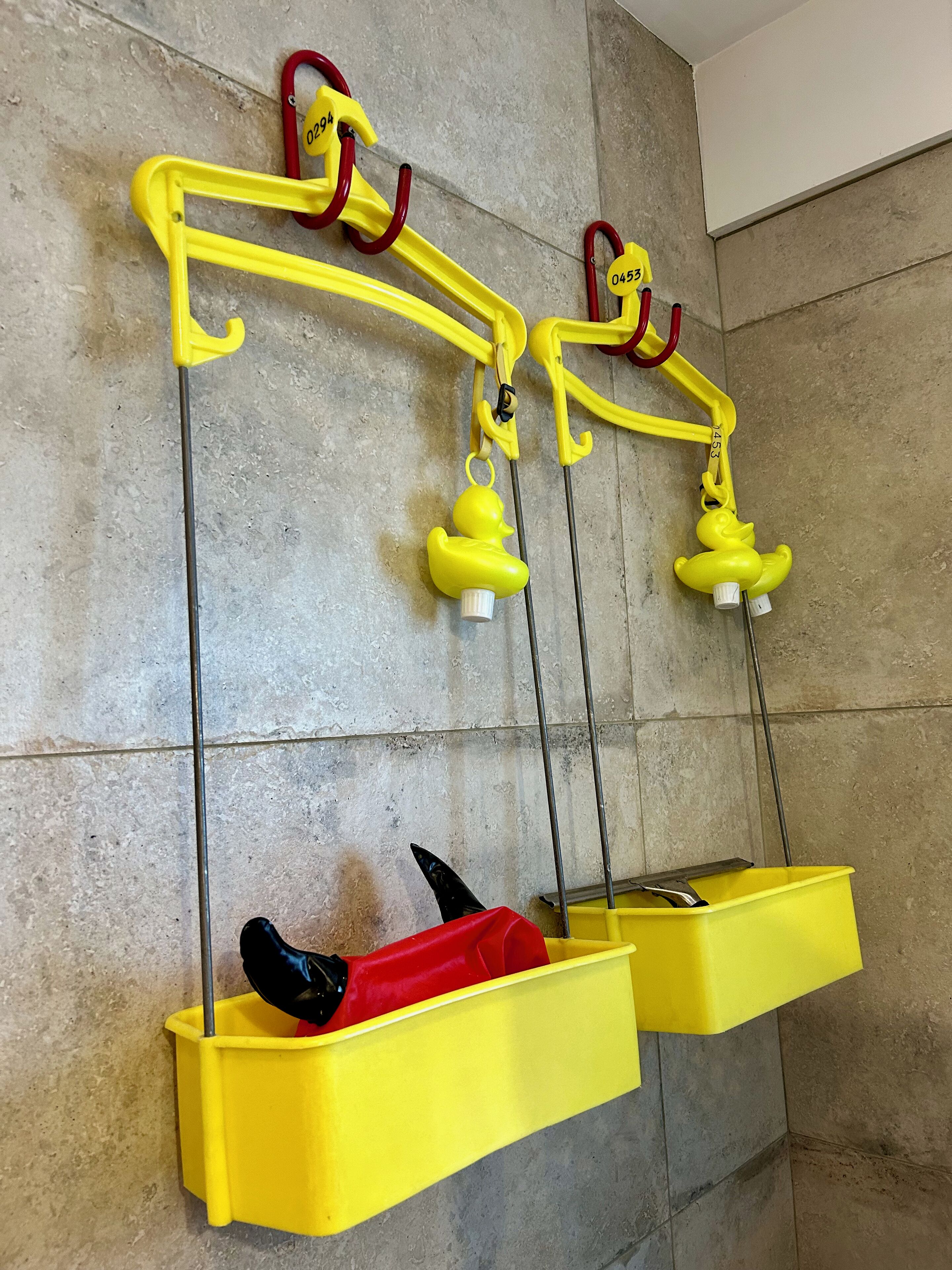 A bathroom with yellow towel racks, a red and black towel, and a yellow trash bin.