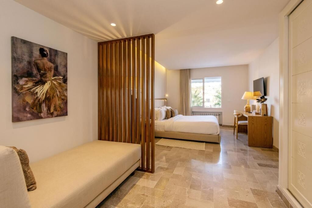 Een hotelkamer met een groot schilderij, een houten scheidingswand, twee bedden, een bureau en een televisie.