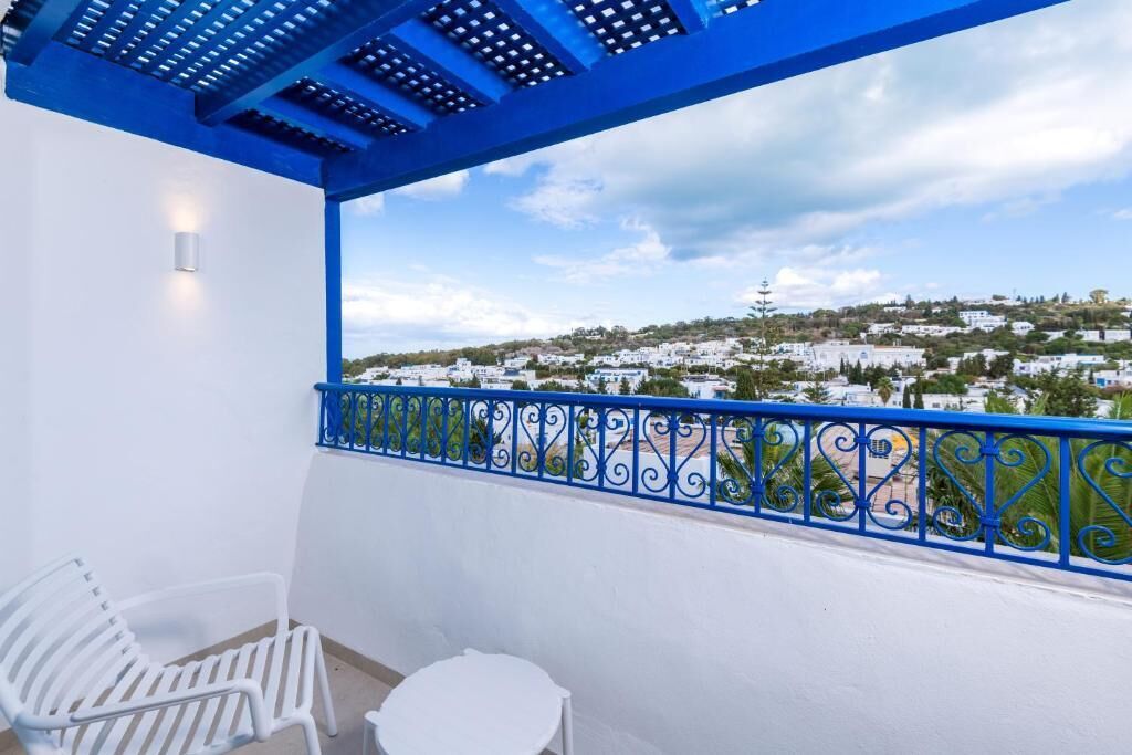 Een balkon met een blauwe reling, witte stoelen en een tafel.