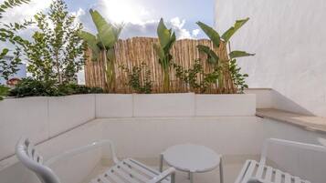 A small outdoor seating area with white plastic chairs and a table, surrounded by plants and a bamboo fence.