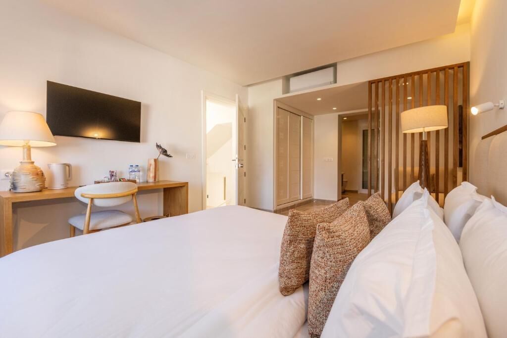 Quarto de hotel com cama, mesa de cabeceira, abajur, televisão e divisória de madeira.
