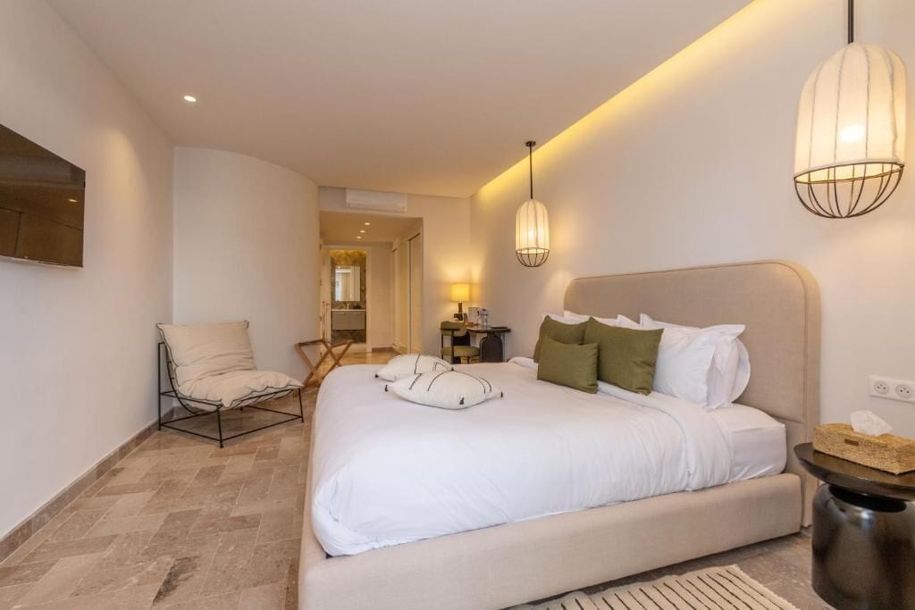 Une chambre d’hôtel moderne, dotée d’un grand lit, d’une chaise, d’un bureau et d’un luminaire suspendu.