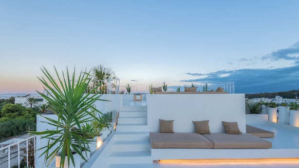 A rooftop terrace with a minimalist design, featuring a sofa with cushions, a staircase, and potted plants.